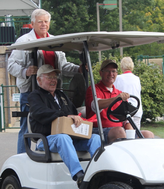 men sitting in golf cart smilingwith a man holding on the back of cart