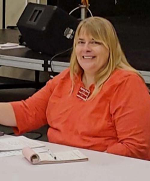 woman in orange shirt sitting at a table taking notes
